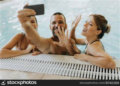 Handsome young people relaxing in the indoor swimming pool and taking selfie with mobile phone