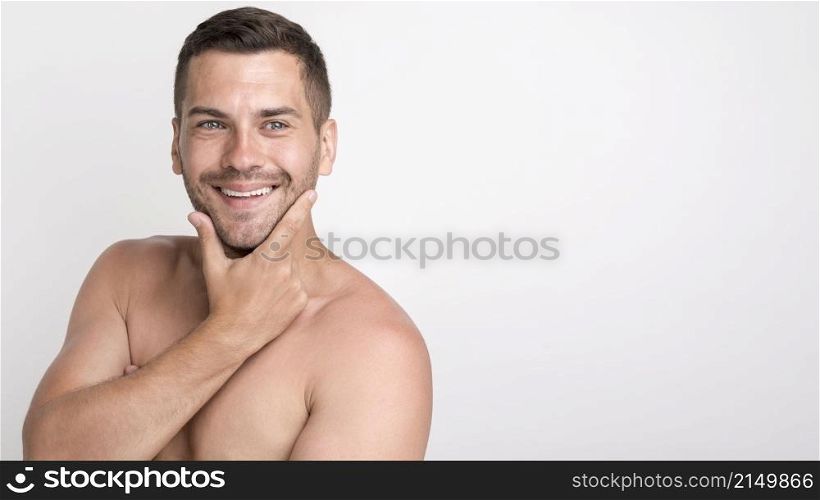 handsome young smiling man looking camera keeping hand chin while standing against white wall