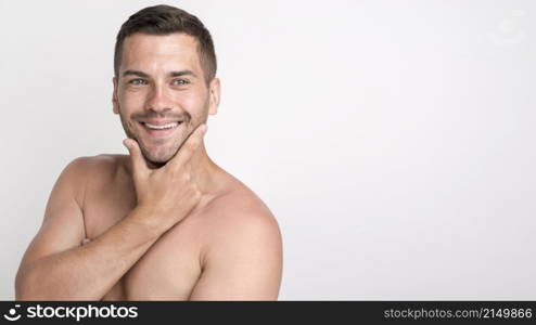 handsome young smiling man looking camera keeping hand chin while standing against white wall