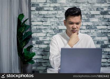 Handsome young thinking while serious working at home with laptop on desk