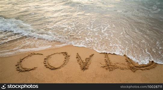 Handwriting COVID on sand and foam wave on beach. Coronavirus concept.