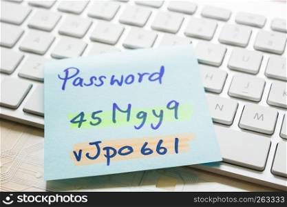 Handwriting passwords with highlight colors written on blue paper note on top of modern white keyboard with wooden office table on background. Login access, data privacy and cyber security concepts.