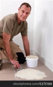 Handyman spreading adhesive over an old tiled floor