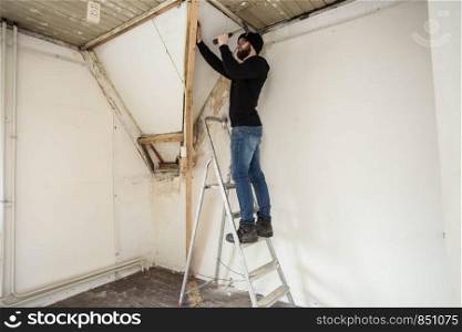 Handyman standing on a ladder and renovating a home, using tools like a hammer concept renovating new home. Handyman standing on a ladder and renovating a home, using tools like a hammer