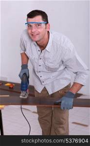 Handyman wearing safety goggles and cutting a piece of wooden flooring with a jigsaw