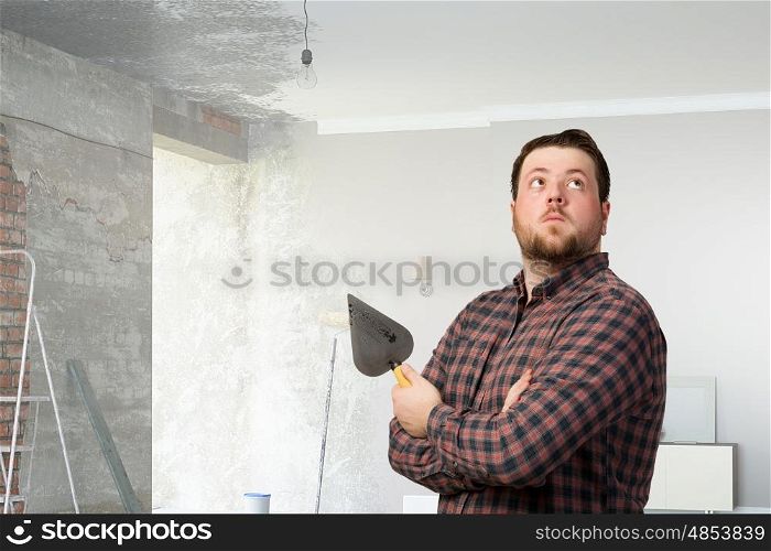 Handyman with tool in interior. Good looking caucasian manual worker with spatula tool inside house. Mixed media