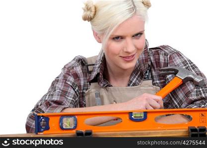 handywoman wearing a checked shirt and holding a hammer behind a level