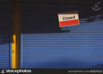 Hanging closed sign board in front of blue shutter door of grocery with sunlight and shadow on surface in vintage tone style