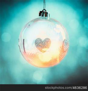 Hanging glass Christmas ball with heart and bokeh lighting on turquoise blue background