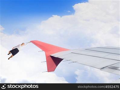 Hanging on edge. Young businesswoman hanging on edge of airplane wing