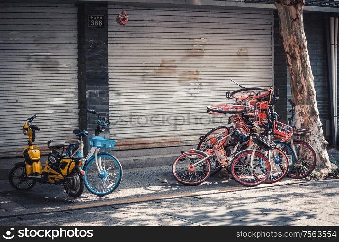 Hangzhou, China - Novemeber 09, 2019: Pile of abandoned broken share electric bicycles on the sidewalk as a result of the bike-share oversupply.. pile of electric bikes on the sidewalk, Hangzhou