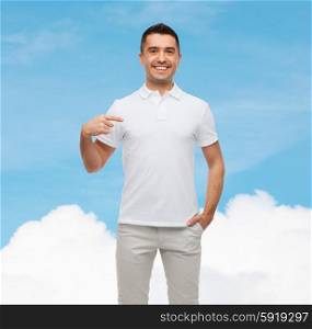happiness, advertisement, fashion, gesture and people concept - smiling man in t-shirt pointing finger on himself over blue sky and cloud background