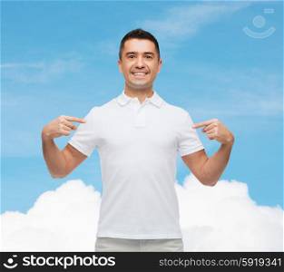 happiness, advertisement, fashion, gesture and people concept - smiling man in t-shirt pointing fingers on himself over blue sky and cloud background