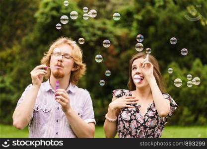 Happiness and carefree concept. Young woman and man having fun blowing soap bubbles together in park, green blurred background. Couple blowing soap bubbles, having fun
