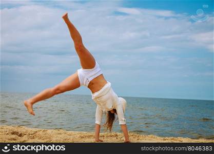 Happiness and craziness. Smiling crazy girl have fun outdoor. Young attractive long haired woman playing on summer beach, doing cartwheel