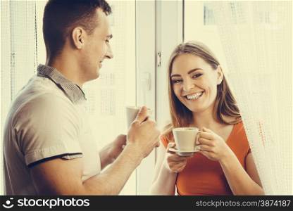 Happiness and healthy relationship concept. Attractive couple drinking tea or coffee together at home, man and woman holding cups with hot beverage at home