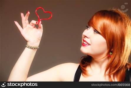 Happiness and love concept. Happy redhair woman smiling girl holding valentine red heart on gray. Valentines day.