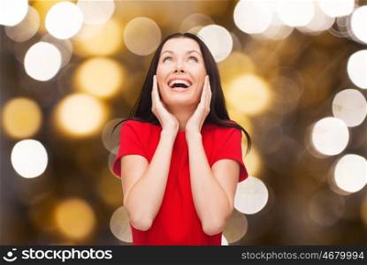 happiness and people concept - amazed laughing young woman in red dress looking up over lights background. amazed laughing woman in red dress looking up