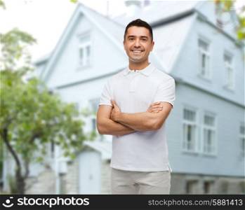 happiness and people concept - smiling man in white t-shirt with crossed arms over house background
