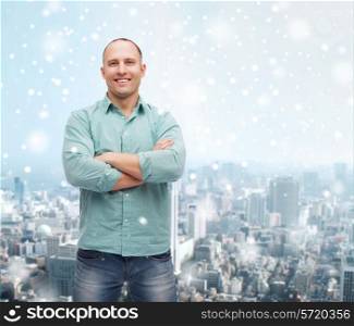 happiness and people concept - smiling man with crossed arms standing over snow and city background