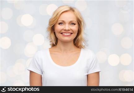 happiness and people concept - smiling woman in blank white t-shirt over holidays lights background. smiling woman in blank white t-shirt