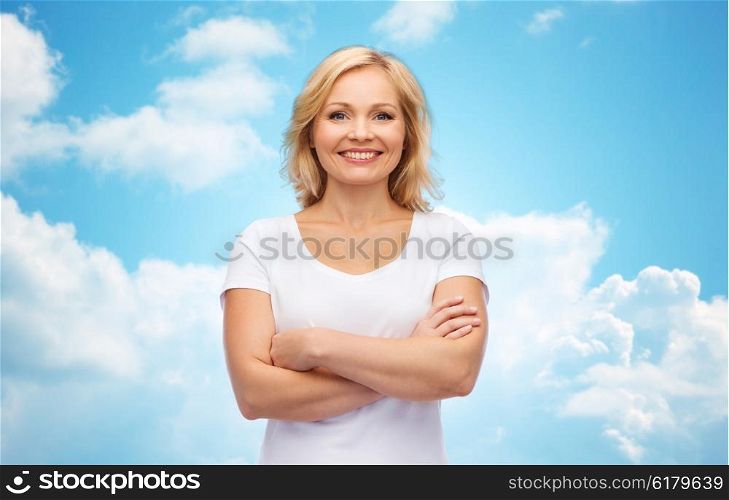 happiness and people concept - smiling woman in blank white t-shirt with crossed arms over blue sky and clouds background. smiling woman in blank white t-shirt
