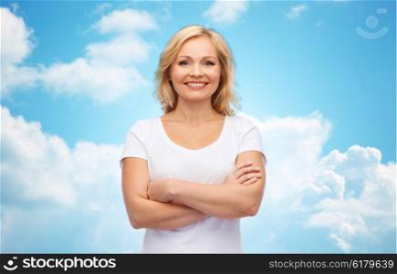 happiness and people concept - smiling woman in blank white t-shirt with crossed arms over blue sky and clouds background. smiling woman in blank white t-shirt