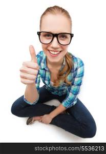 happiness and people concept - smiling young woman in casual clothes and eyeglasses sitiing on floor and showing thumbs up