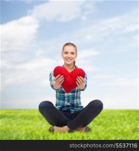 happiness and people concept - smiling young woman in casual clothes sitiing on floor and holding red heart
