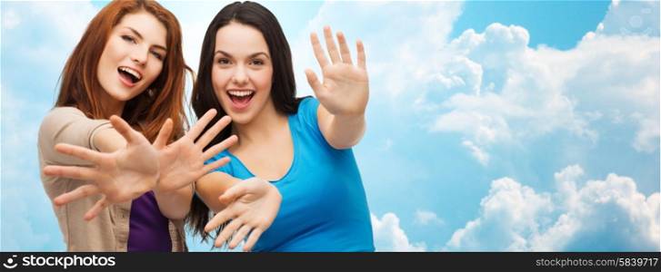 happiness and people concept - two smiling girls or young women showing their palms over blue sky with clouds background. happy girls or young women showing their palms