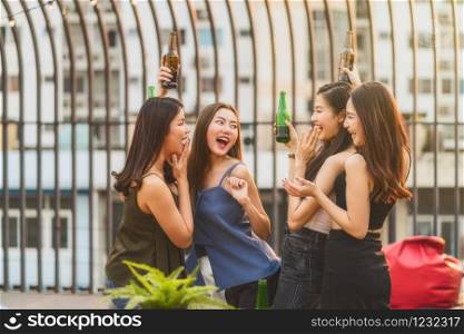 Happiness Asian Girl Friend Group celebrating and dancing together with her beer bottle at sunset time on rooftop of downtown hotel or nightclub,hens night,holiday, or yearly anniversary party concept