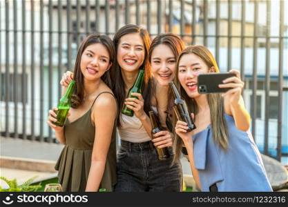Happiness Asian Girl Friend Group taking a selfie while celebrating and dancing together with her beer bottle at sunset time on rooftop, hens night, holiday, or yearly anniversary party concept