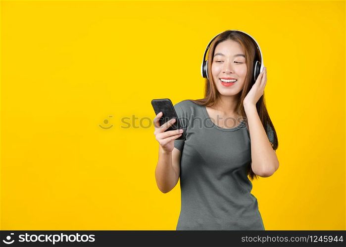 Happiness Asian smiling young woman wearing technology wireless headphones for listening the music via smart mobile phone on isolated yellow color background, Lifestyle and leisure with hobby concept