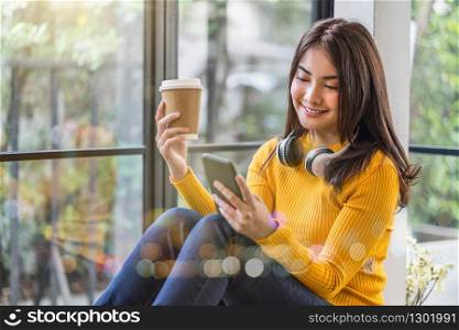 Happiness Asian smiling young woman wearing technology wireless headphones for listening the music via smart mobile phone infront of coffee shop or coworking space, Lifestyle and leisure concept