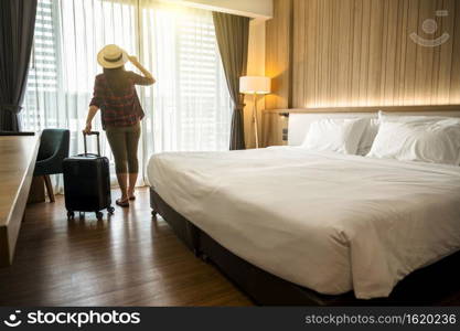 Happiness Asian traveler woman standing with baggage in bedroom of hotel or hostel when traveling on her holiday, luxury interior bedroom design, tourism and travel concept