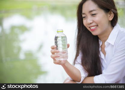 Happiness Beautiful asian chinese women holding mineral water bottle. Young Woman Drinking Water from bottle in green garden Park. Asian female drinking water bottle healthy person happy and smiling