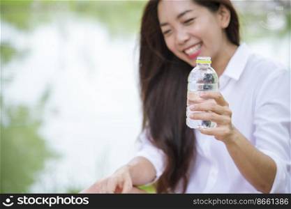 Happiness Beautiful asian chinese women holding mineral water bottle. Young Woman Drinking Water from bottle in green garden Park. Asian female drinking water bottle healthy person happy and smiling
