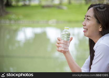 Happiness Beautiful asian chinese women holding mineral water bottle. Young Woman Drinking Water from bottle in green garden Park. Asian female drinking water bottle healthy person happy and smiling