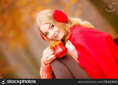 Happiness carefree and fall concept. Young happy woman relaxing in the autumn park on bench enjoying hot drink holding red mug with warm beverage. Orange leaves background