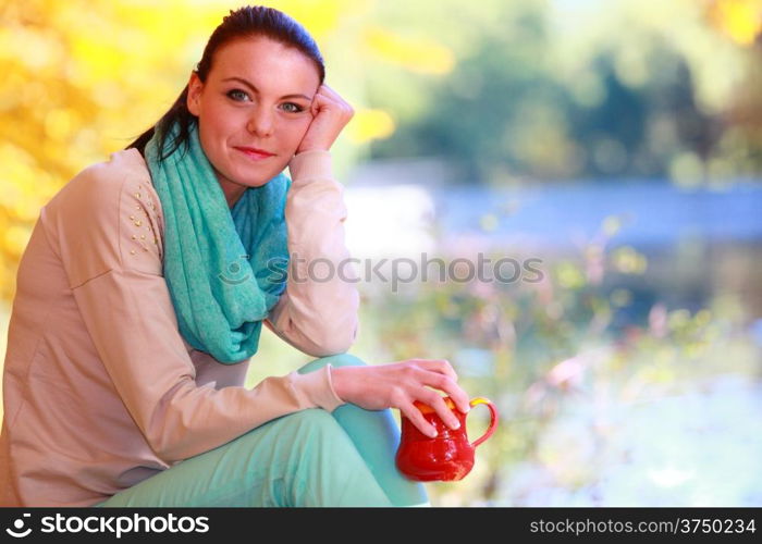 Happiness carefree and nature. Young happy woman relaxing in the autumn park enjoying hot drink coffee or tea, holding red mug with warm beverage. Yellow leaves background