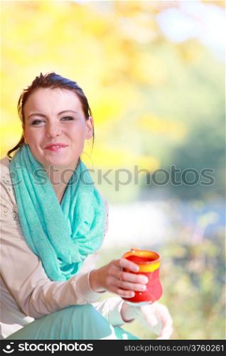 Happiness carefree and nature. Young happy woman relaxing in the autumn park enjoying hot drink coffee or tea, holding red mug with warm beverage. Yellow leaves background