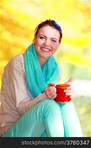 Happiness carefree and nature. Young happy woman relaxing in the autumn park enjoying hot drink coffee or tea, holding red mug with warm beverage. Yellow leaves background