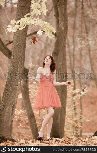 Happiness carefree. Young pretty woman relaxing in the autumn park throwing leaves up in the air with arms raised up, smiling elated expression. Beautiful girl outdoor. Vintage photo, sepia tone