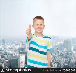 happiness, childhood and people concept - smiling little boy in casual clothes showing thumbs up over city background