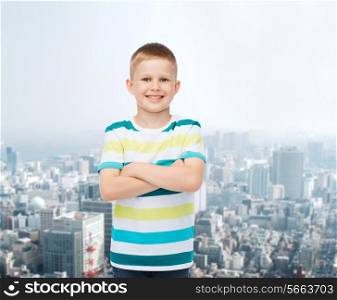 happiness, childhood and people concept - smiling little boy in casual clothes with crossed arms over city background