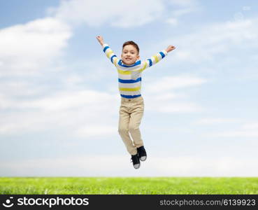 happiness, childhood, freedom, movement and people concept - happy little boy jumping in air over blue sky and grass background