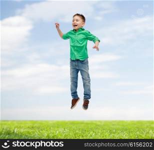 happiness, childhood, freedom, movement and people concept - happy little boy jumping in air over blue sky and grass background