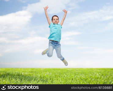 happiness, childhood, freedom, movement and people concept - happy little girl jumping in air over blue sky and grass background