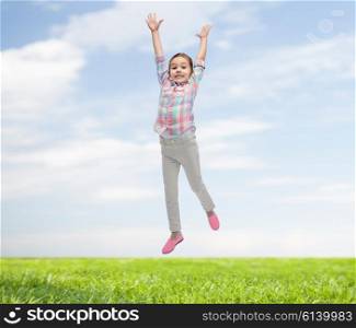 happiness, childhood, freedom, movement and people concept - happy little girl jumping in air over blue sky and grass background