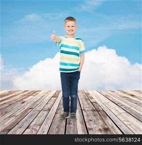 happiness, childhood, gesture and people concept - smiling little boy showing thumbs up over blue sky and wooden floor background